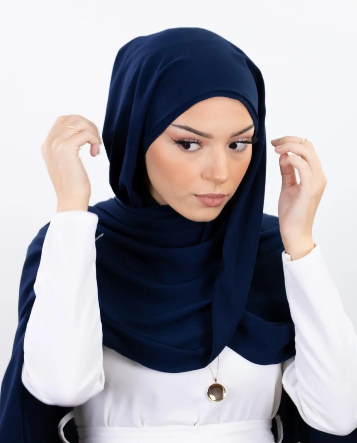 Une femme portant un hijab en mousseline bleu marine et un haut blanc, regardant directement l'appareil photo.