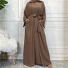 A full-length, flowing brown abaya or kaftan garment with a tied waist detail displayed against a white paneled wall.