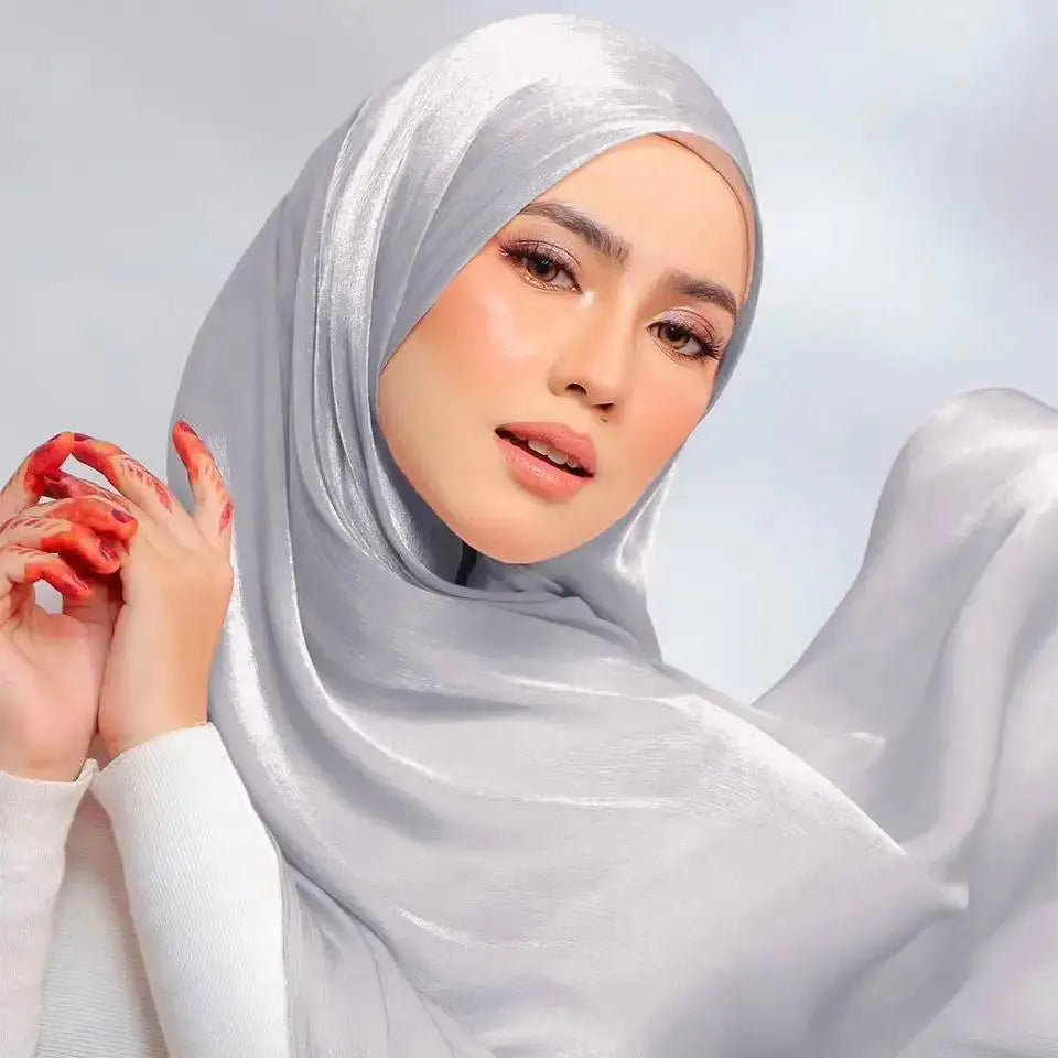 Una mujer vistiendo un chal de hijab de gasa arrugada y brillante plateado con mangas blancas.