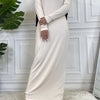 Langes beige Maxi-Abaya-Kleid mit langen Ärmeln und schwarzem Hijab vor weißer Paneelwand.