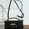 A black crocodile pattern shoulder bag with a gold chain strap displayed on a clear glass stand.