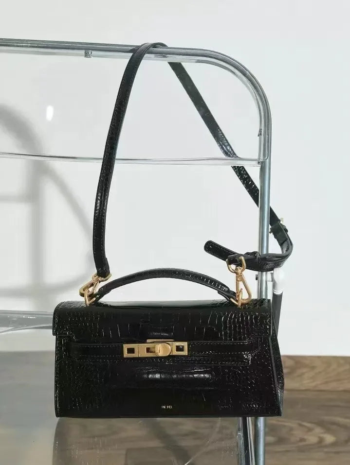 A black crocodile pattern shoulder bag with a gold chain strap displayed on a clear glass stand.