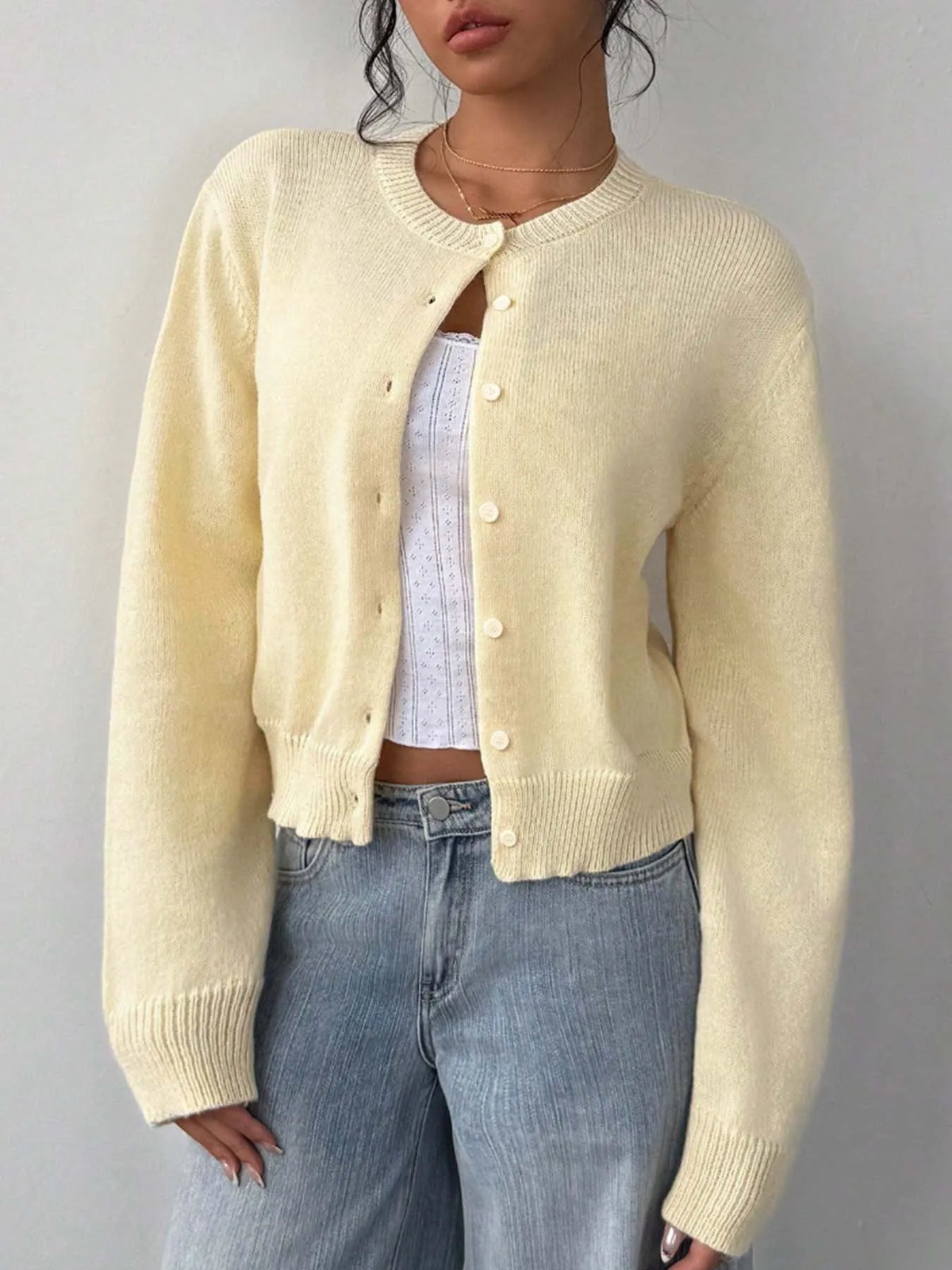Une femme portant un pull en tricot jaune pâle sur un haut blanc et un jean.