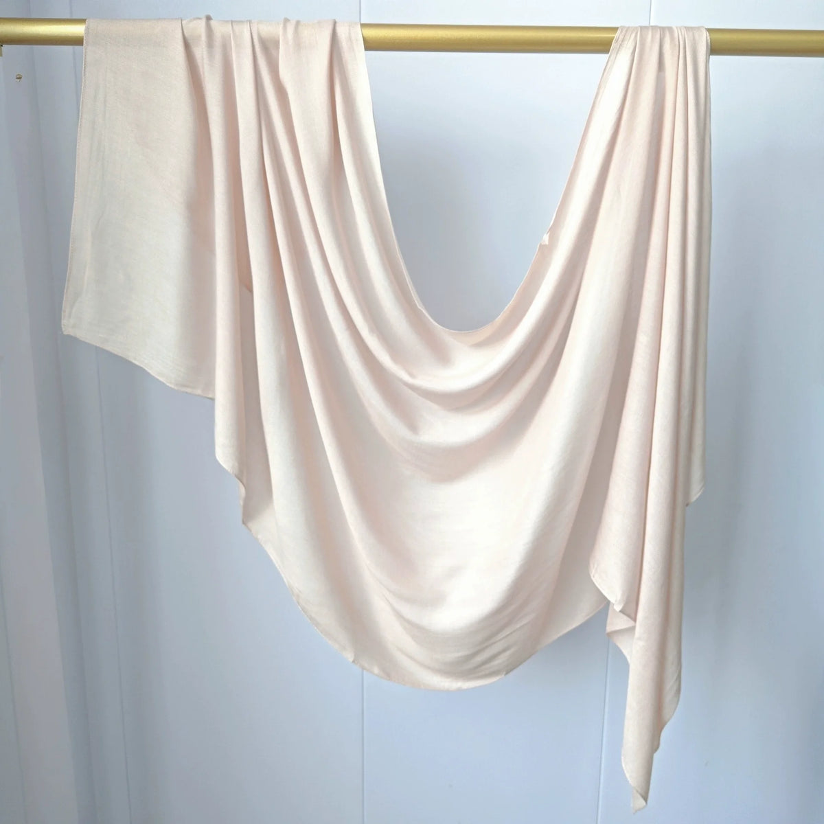 Foulard modal rose pâle fluide drapé sur un cintre or contre fond blanc.