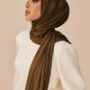 Eine Frau trägt einen olivgrünen Modal-Jersey-Hijabschal aus Baumwolle und einen weißen Strickpullover.