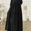 Eine Frau trägt ein elegantes schwarzes muslimisches Abaya Kaftankleid mit lila Hijab und silbernem Armreif.