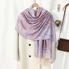 Una chal vintage de bordado paisley rosa claro y morado drapeada sobre un abrigo blanco.
