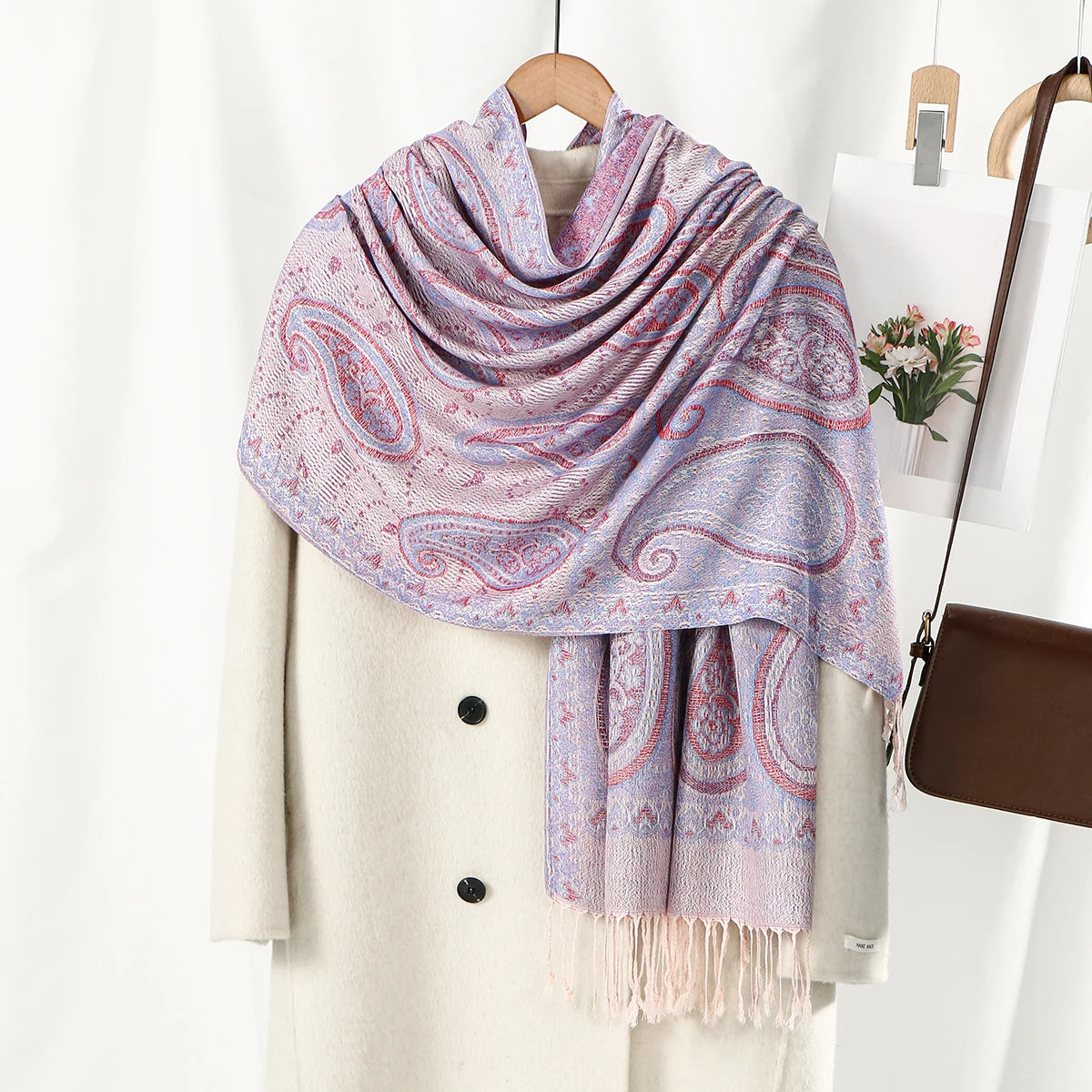 Una chal vintage de bordado paisley rosa claro y morado drapeada sobre un abrigo blanco.