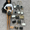 Muñeca de moda con cabello negro junto a varios accesorios de bolsos negros y dorados.