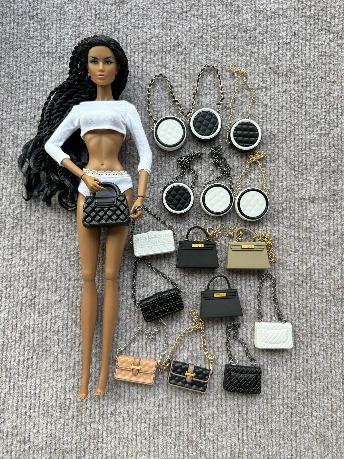 Muñeca de moda con cabello negro junto a varios accesorios de bolsos negros y dorados.