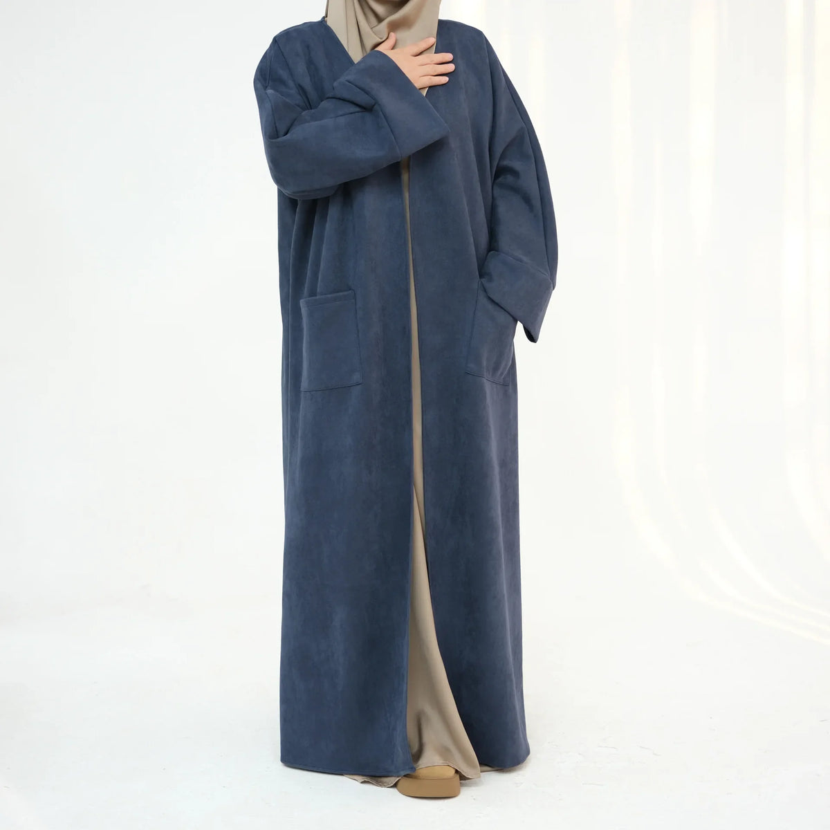 A woman wearing an elegant navy blue abaya trench coat over a beige garment.