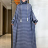 Una mujer vistiendo una abaya de algodón azul oscuro con un pañuelo floral, de pie en un ambiente interior bien iluminado.