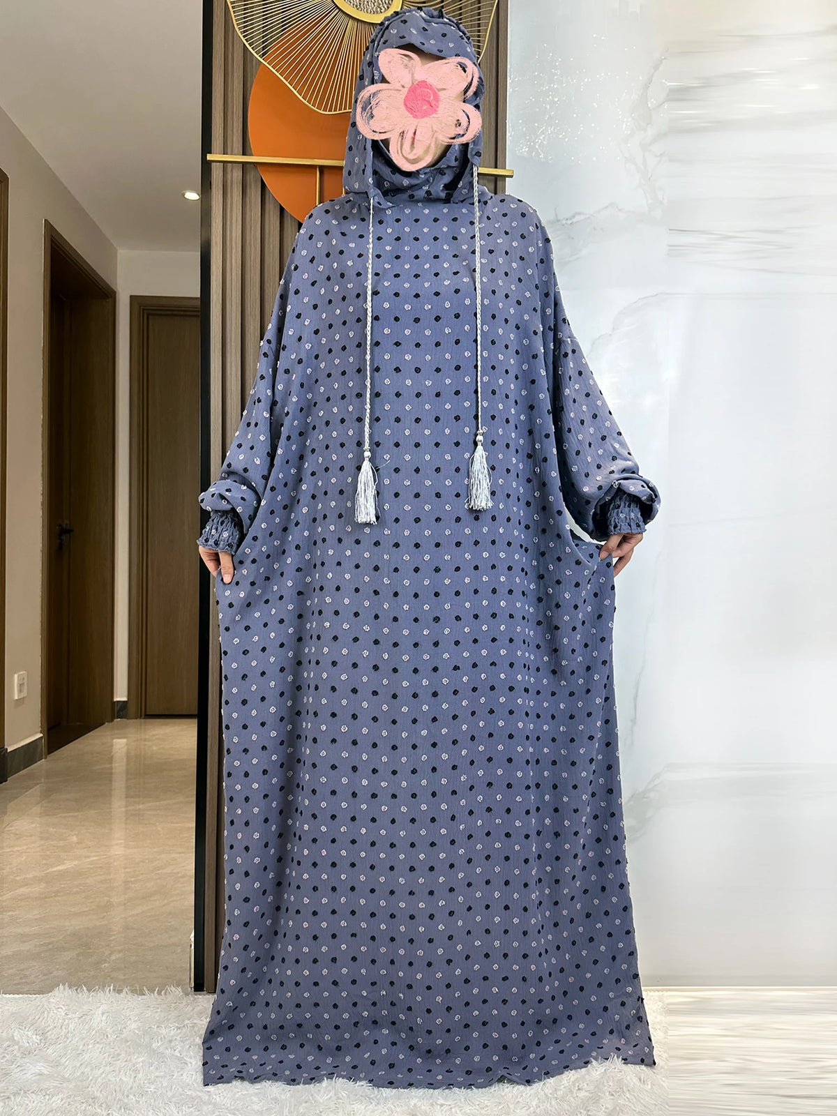 Una mujer vistiendo una abaya de algodón azul oscuro con un pañuelo floral, de pie en un ambiente interior bien iluminado.