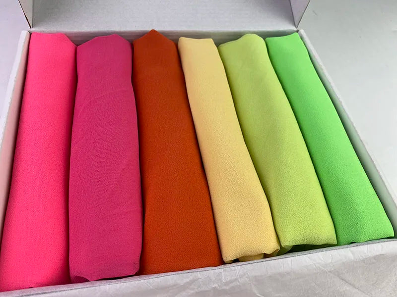 Eine Box mit sechs gerollten Chiffon-Hijab-Schals in Rosa-, Orange-, Gelb- und Grüntönen.