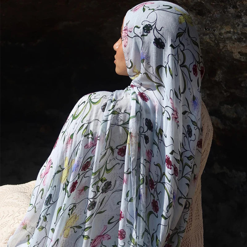 Une femme portant un hijab floral aquarelle bleu clair et rose, vue de profil.