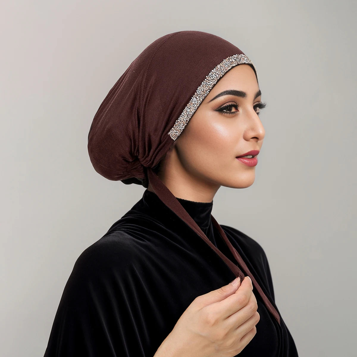 Eine Frau trägt einen dunkelbraunen Samt-Hijab mit funkelndem Strassbesatz und einem schwarzen Oberteil.