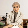 Une femme portant un hijab instant beige et un blazer beige clair est assise sur une chaise en bois.