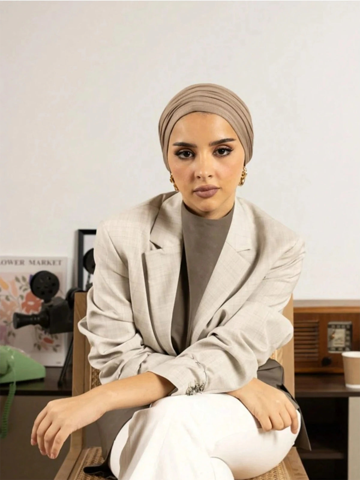 Une femme portant un hijab instant beige et un blazer beige clair est assise sur une chaise en bois.