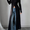 Eine Frau trägt einen schwarzen gerippten Strick-Maxi-Cardigan über blauen Jeans und weiße Sneaker.