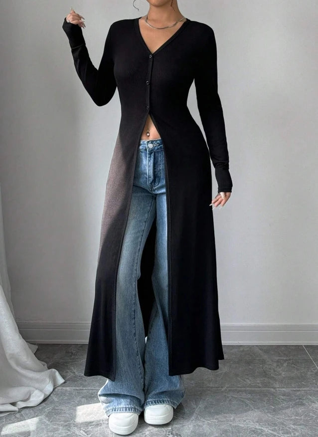 Eine Frau trägt einen schwarzen gerippten Strick-Maxi-Cardigan über blauen Jeans und weiße Sneaker.