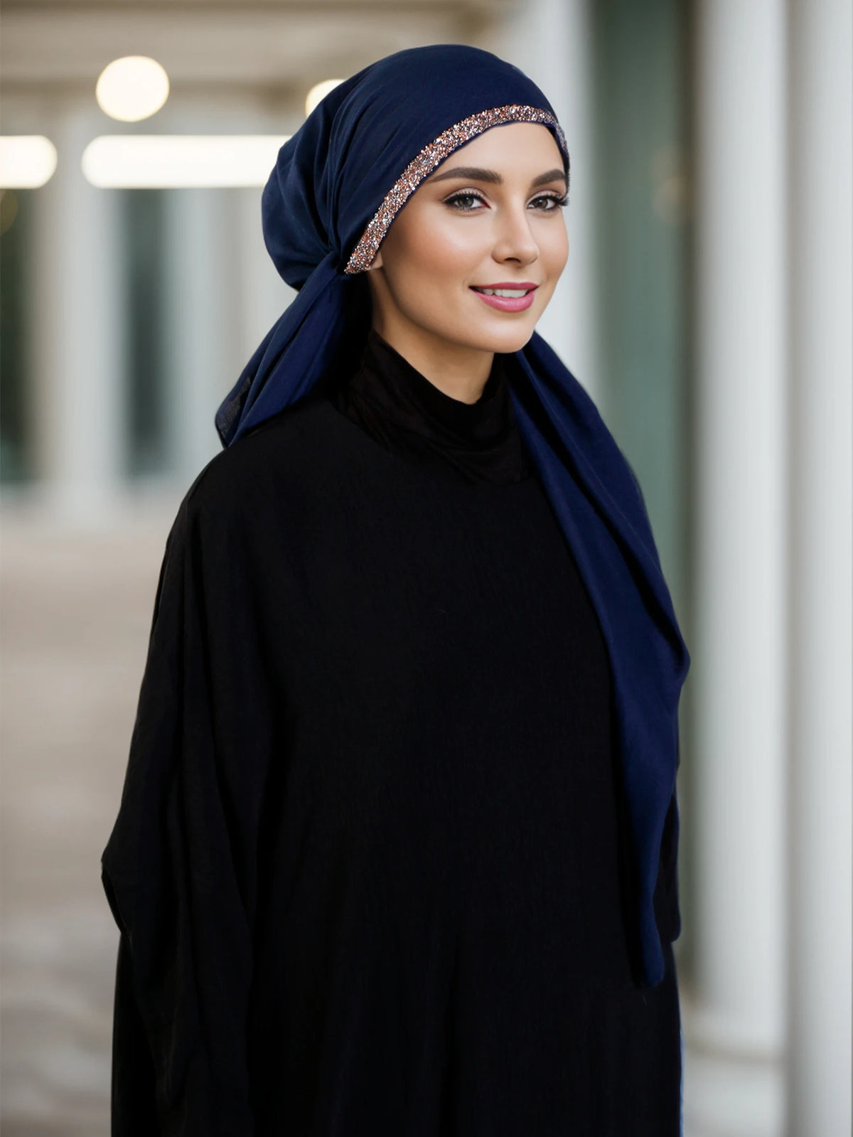 Una mujer vistiendo un hijab azul oscuro y ropa negra con una diadema de diamantes brillantes.