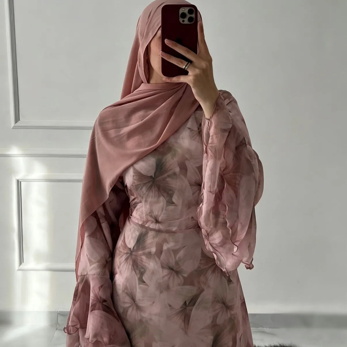 Eine Frau trägt ein fließendes, durchscheinendes Blumenmuster-Abaya und Kaftan in staubiges Rosé.