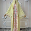 Une longue abaya jaune fluo avec des détails en dentelle florale rose, présentée sur un fond blanc orné.