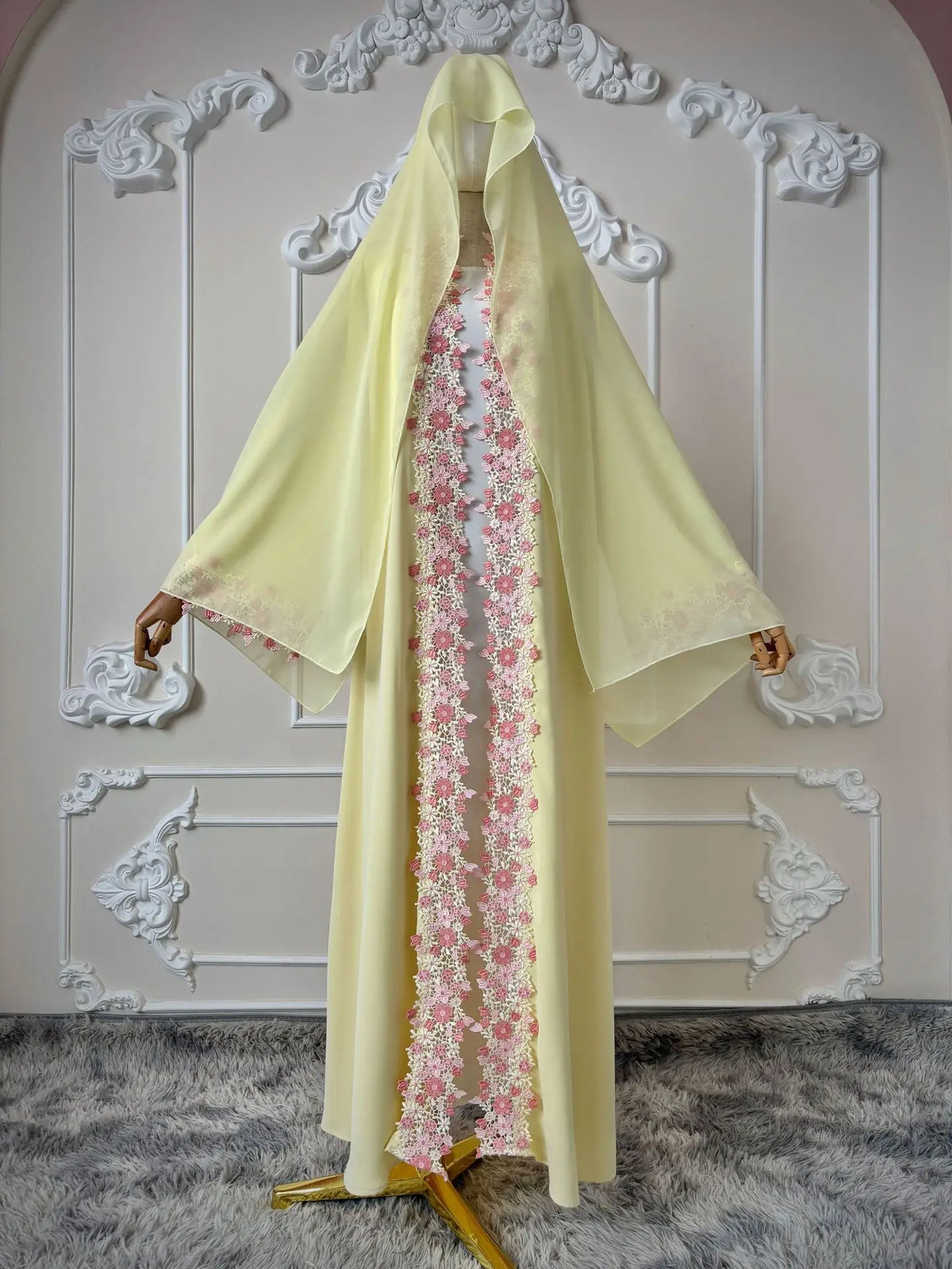 Une longue abaya jaune fluo avec des détails en dentelle florale rose, présentée sur un fond blanc orné.