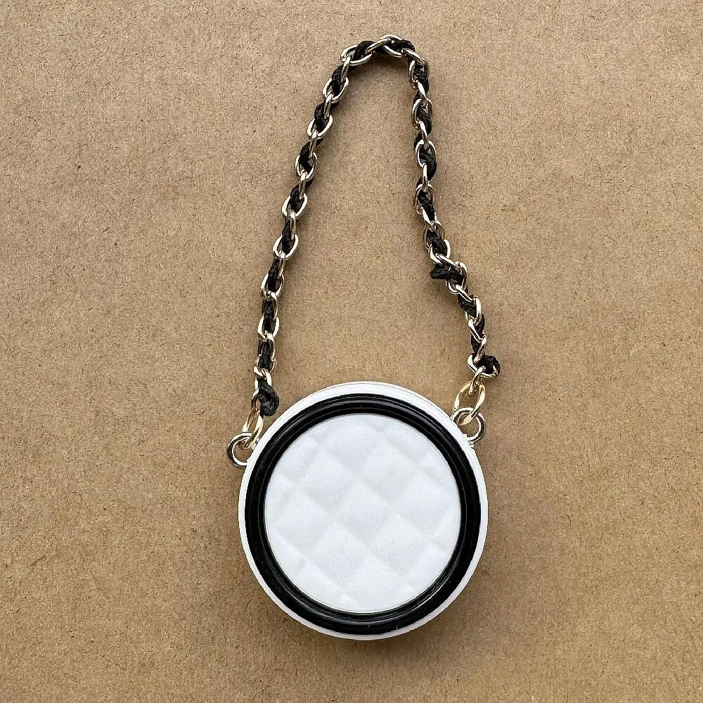 Collar de cadena negra con colgante circular acolchado blanco sobre una superficie marrón.