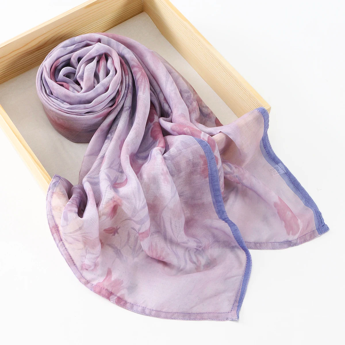 Écharpe de coton à motifs floraux lavande douce roulée et présentée dans un cadre en bois.