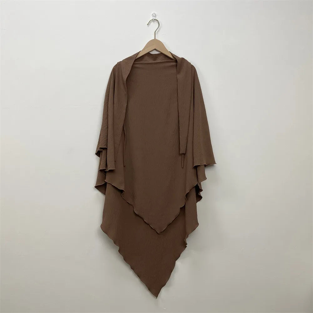 A brown two-layer everyday hijab scarf hanging on a hanger against a white wall.