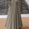 Femme portant une caftan longue, fluide, patchwork vert olive avec plis verticaux et un col beige.