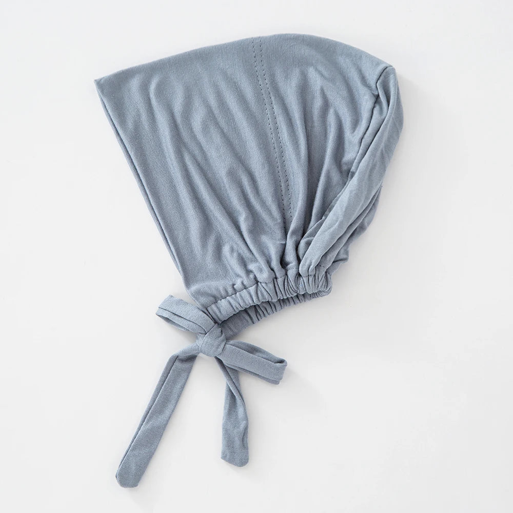 Ein weicher, hellblauer, gebundener innerer Hijab-Bonnet, gefaltet und auf einer weißen Oberfläche präsentiert.