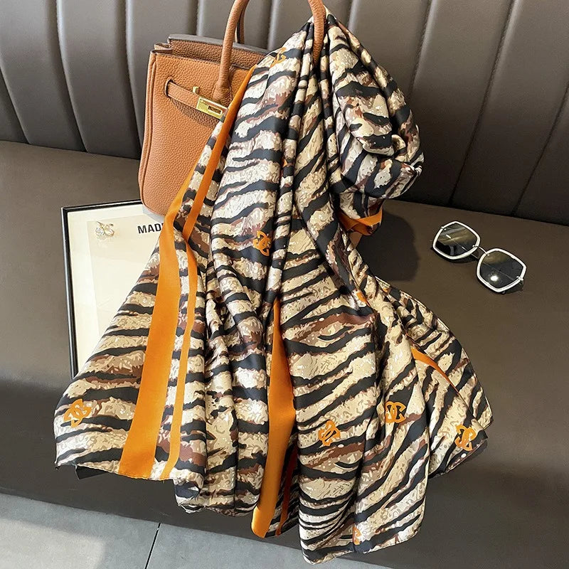 Gemusterter Seidenschal mit braun-schwarzen Zebrastreifen, drapiert neben einer tanfarbenen Ledertasche.