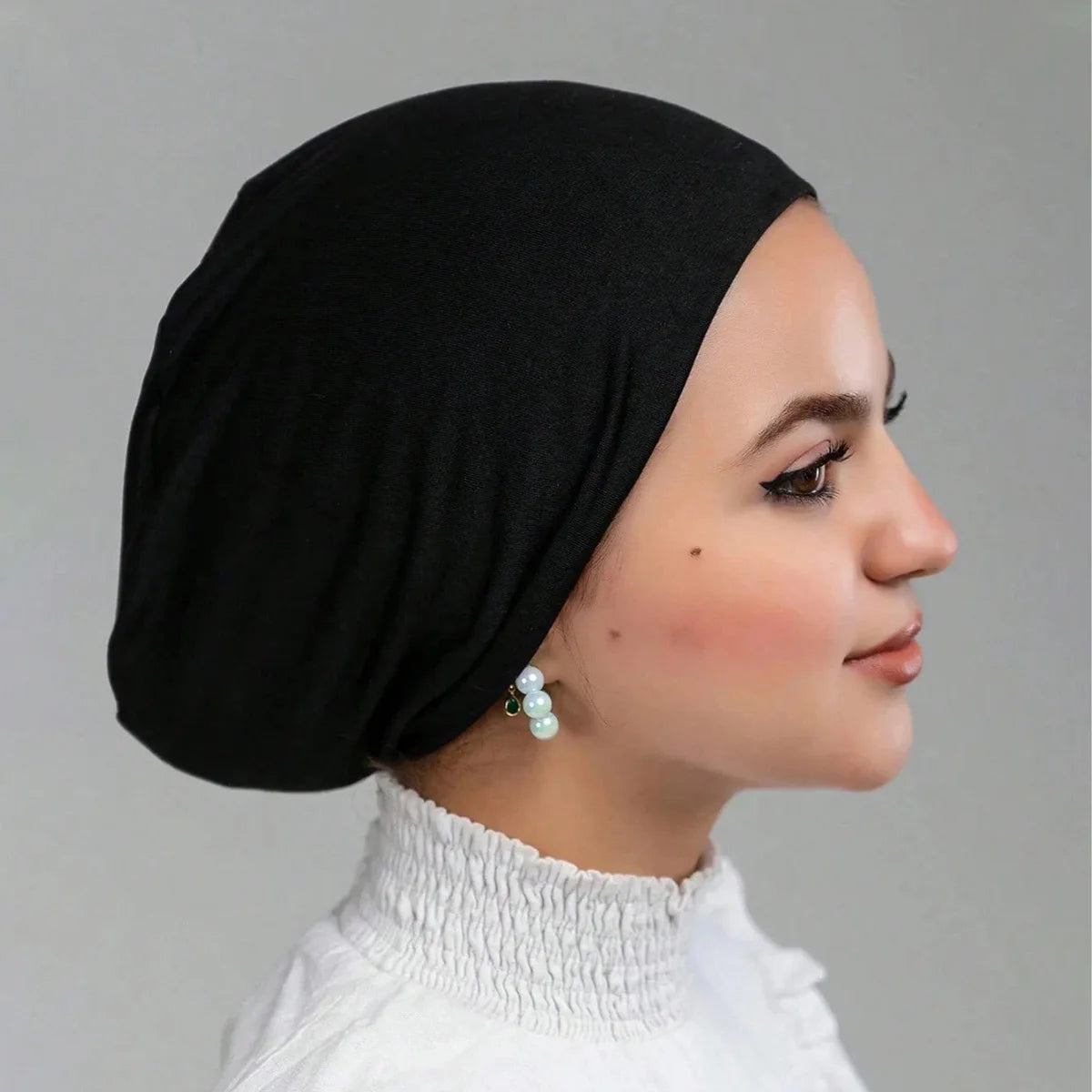 Una mujer vistiendo un gorro de hijab de licra negra y una blusa de cuello alto blanca.