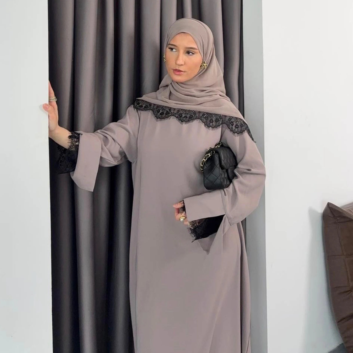 Una mujer vistiendo una modesta abaya gris con detalles de encaje negro y un hiyab a juego.
