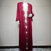 Un largo y fluido vestido kaftan magenta exhibido en un maniquí contra una pared de paneles blancos.