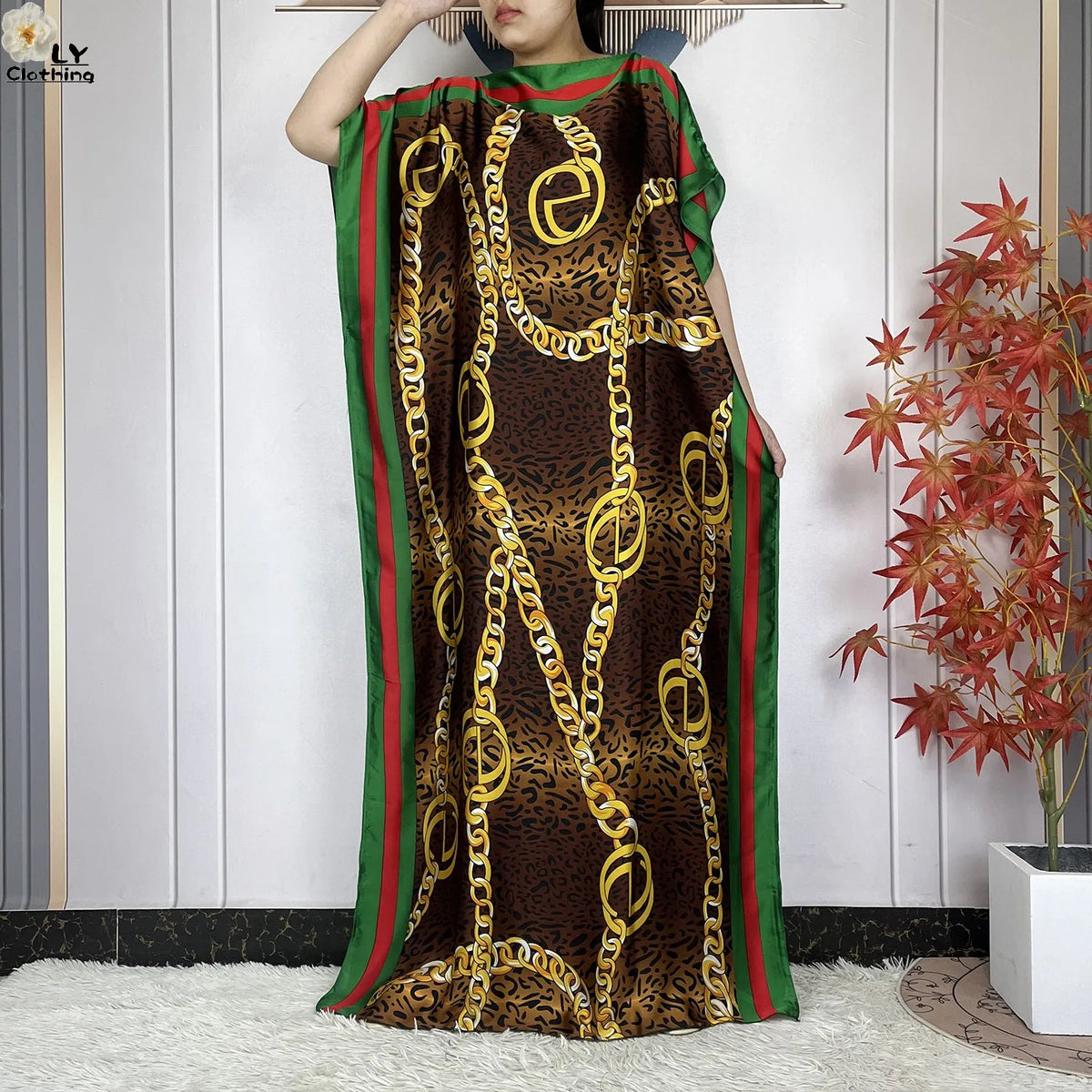 Eine Frau trägt ein braunes Leopardenmuster-Kaftankleid mit grünem Zierrand und goldfarbenen Kettendetails.