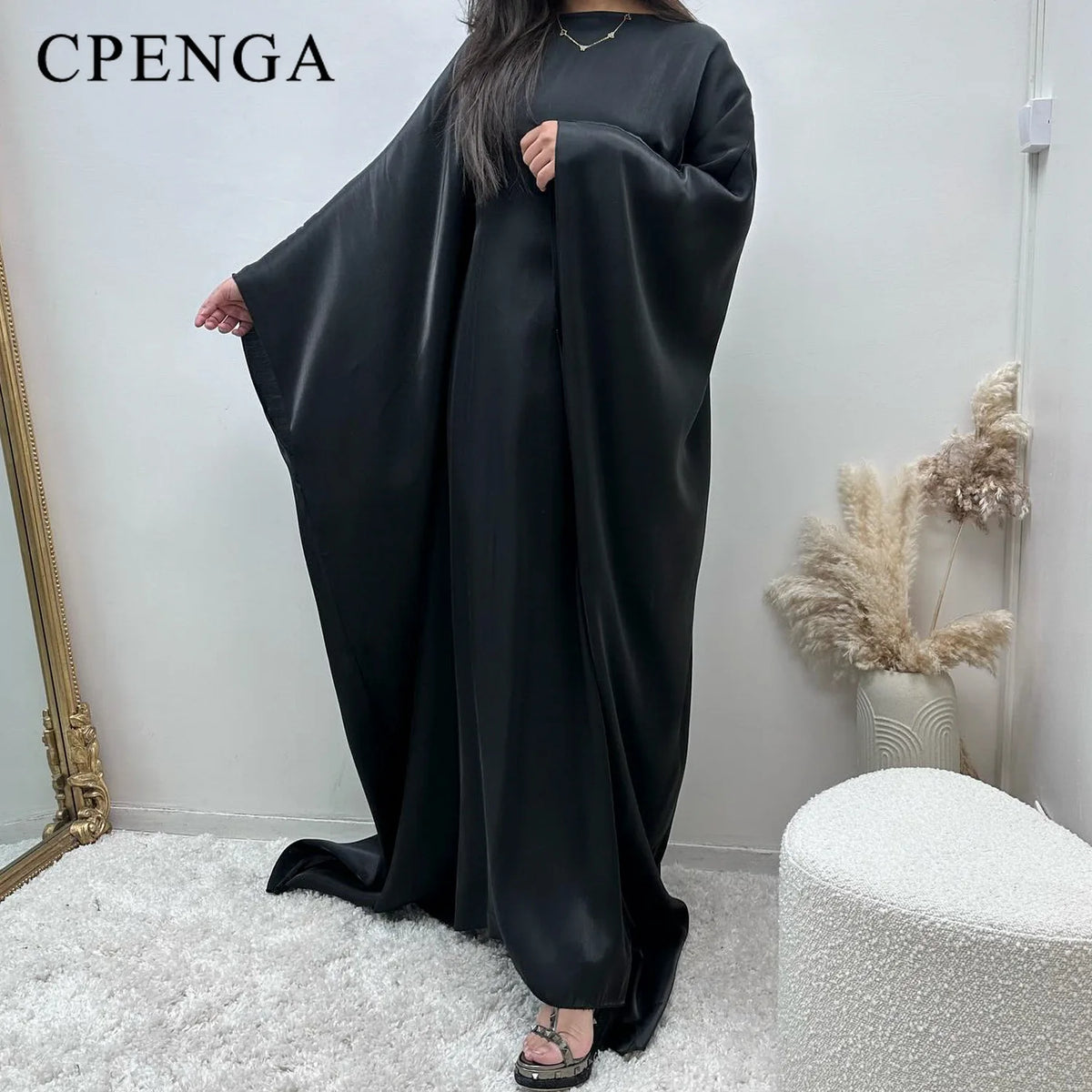 Eine Frau trägt eine elegante schwarze Langarm-Abaya mit fließender Draperie in einem hellen Raum.