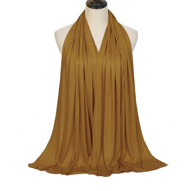 A woman wearing a flowing, olive gold soft modal jersey hijab scarf draped in a V-neck style.