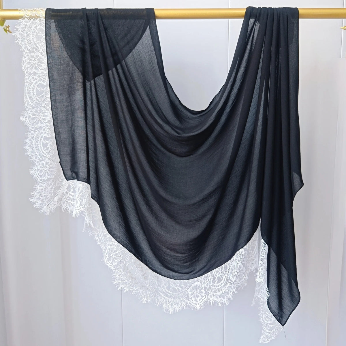 Hijab negro transparente con ribete de encaje blanco colgado en percha de madera.