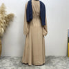 Elegante beige Maxi-Abaya mit dunkelblauen Ärmeln und Kragen vor weißer Wand.