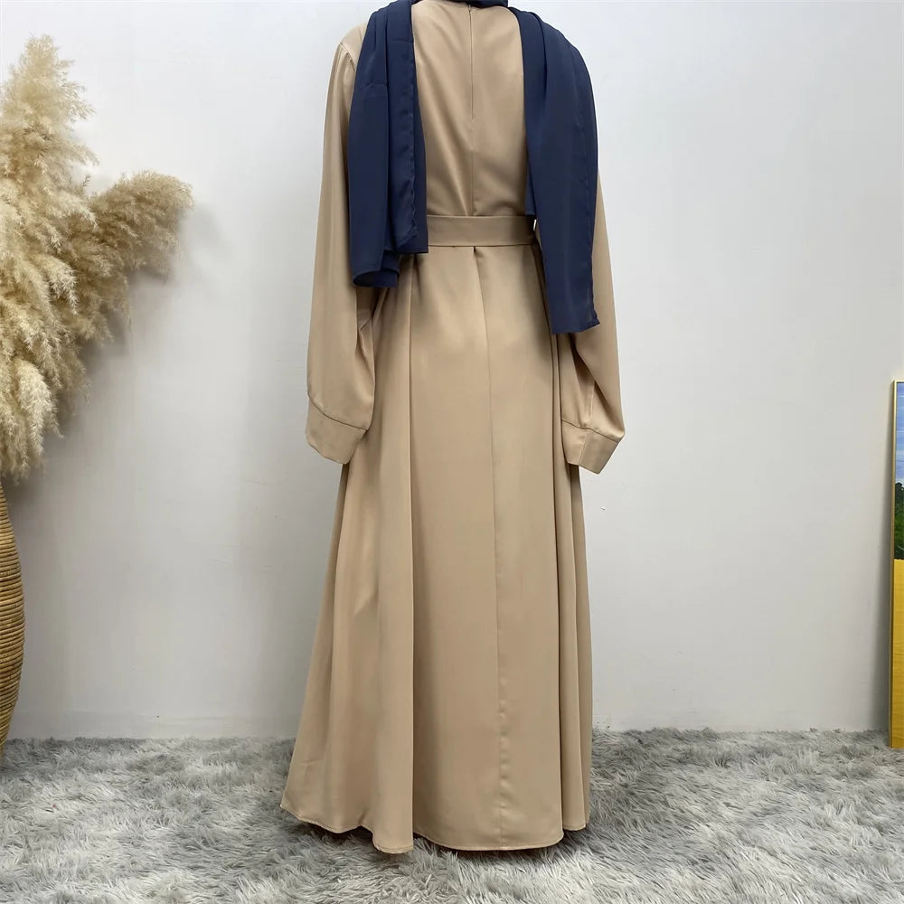 Elegante beige Maxi-Abaya mit dunkelblauen Ärmeln und Kragen vor weißer Wand.
