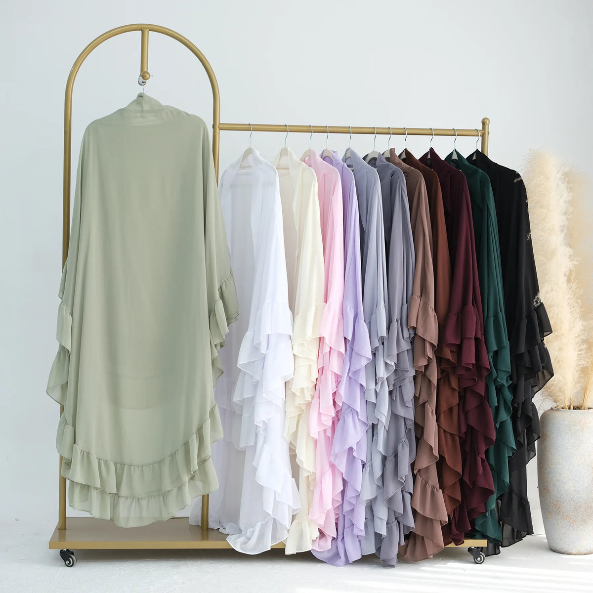 A display of ruffled two-layer chiffon hijabs in various pastel and earth tones hanging on a gold rack.
