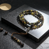 Tasbih de cuentas marrón y amarillo con borlas de luna y estrella sobre una superficie cuadrada gris oscuro.