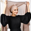 Eine Frau modelliert ein schwarzes Oberteil und einen beigen Chiffon-Hijab mit Hut, der um ihren Kopf drapiert ist.