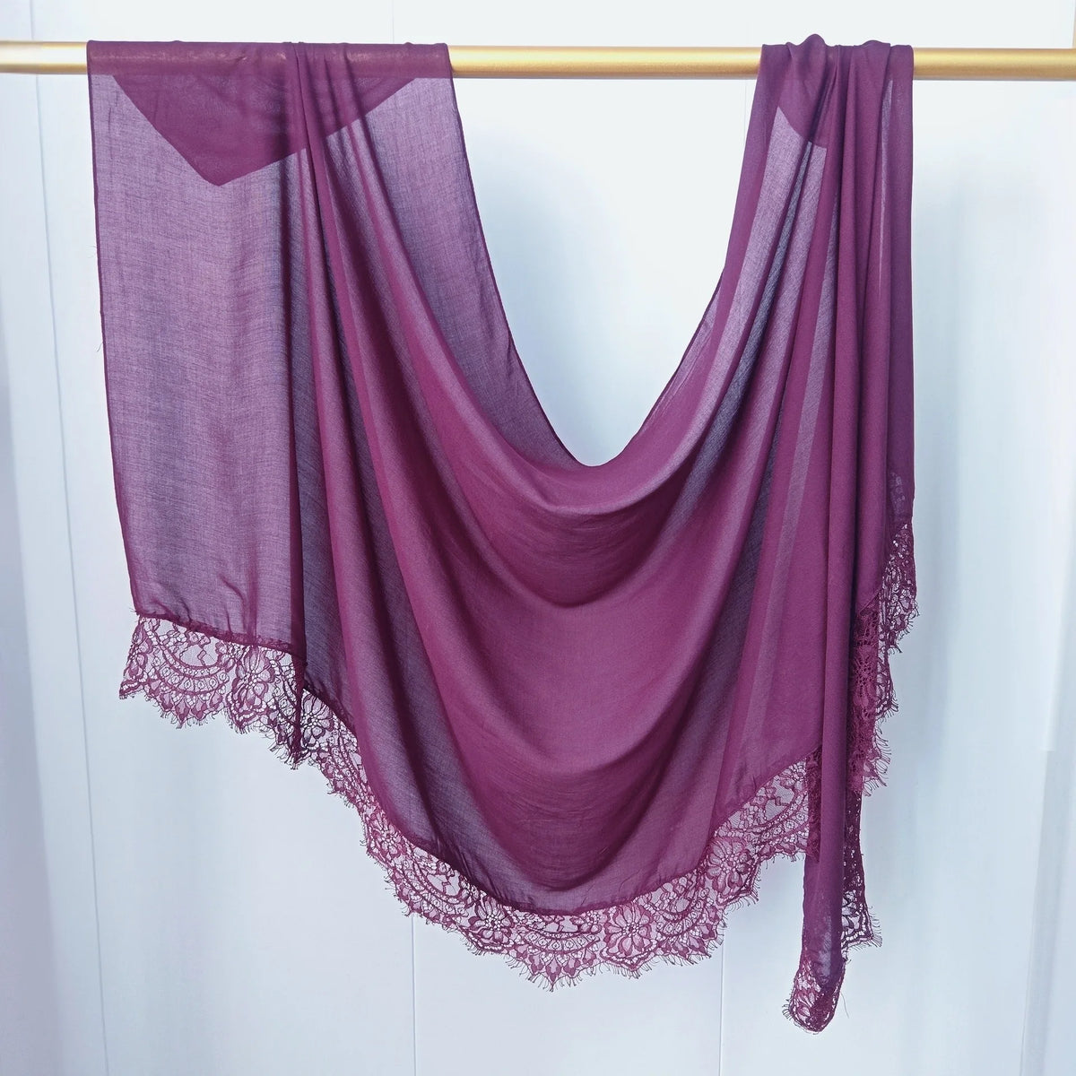 Hijab de encaje morado intenso drapeado sobre un perchero de madera.