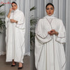 Modelo vistiendo una abaya blanca oversize con ribetes negros y un hiyab a juego, en plano completo.
