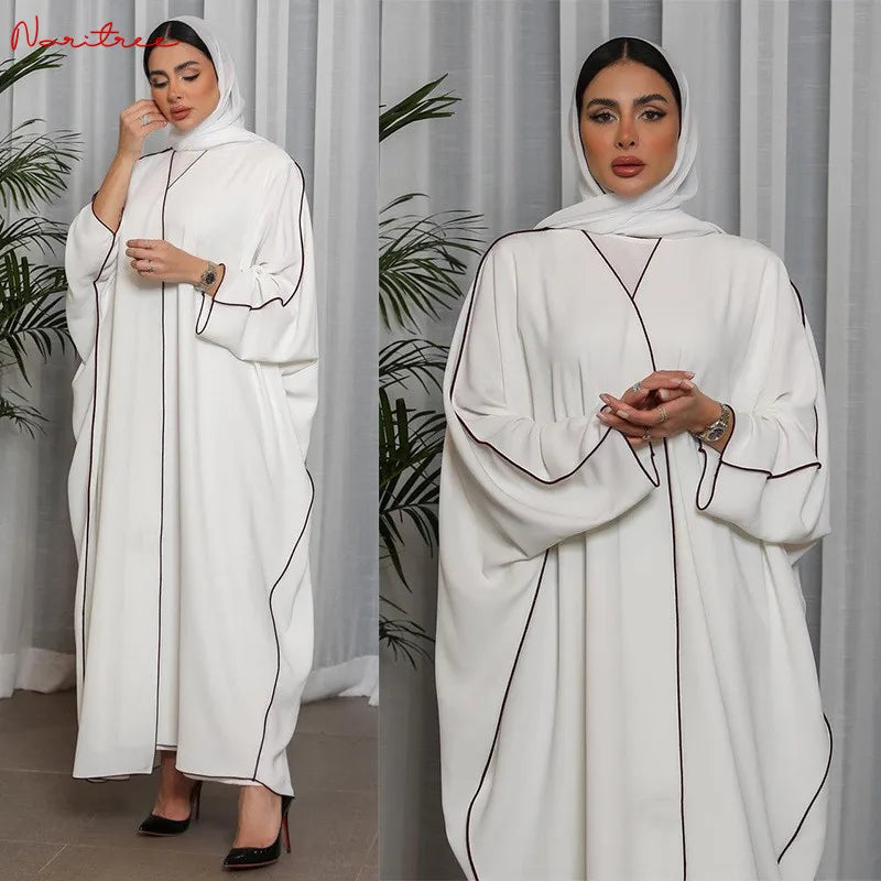 Modelo vistiendo una abaya blanca oversize con ribetes negros y un hiyab a juego, en plano completo.