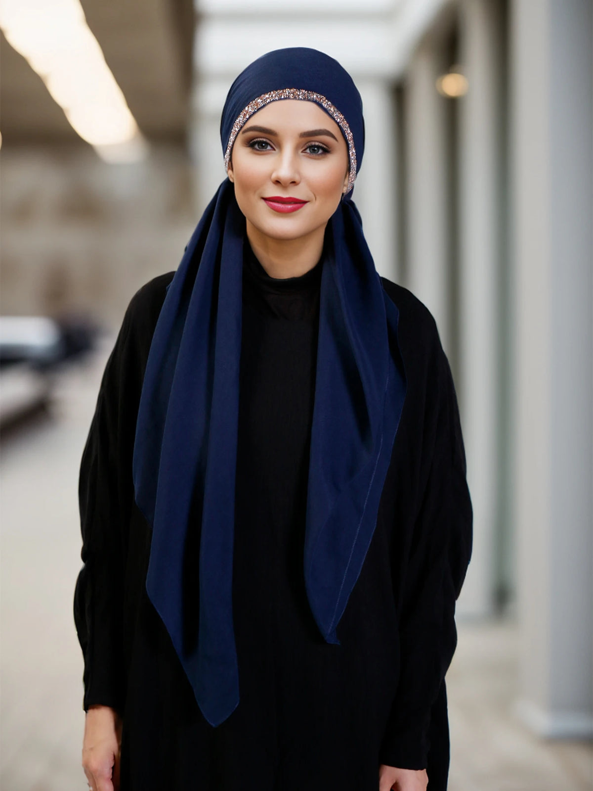Una mujer vistiendo un hiyab azul oscuro y ropa negra con una diadema gorra incrustada de diamantes.